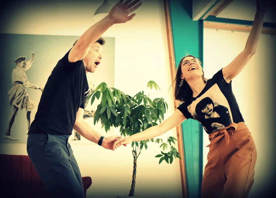 Un couple au studio lève les bras, l’air ébahi et rieur