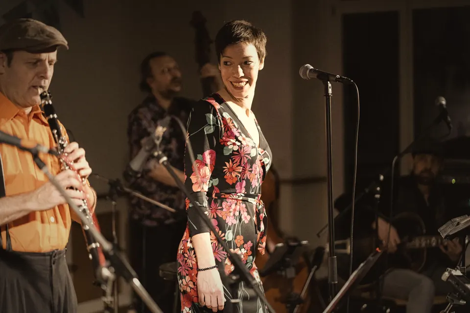 Groupe live sur scène : clarinettiste en chemise orange et chanteuse en robe fleurie