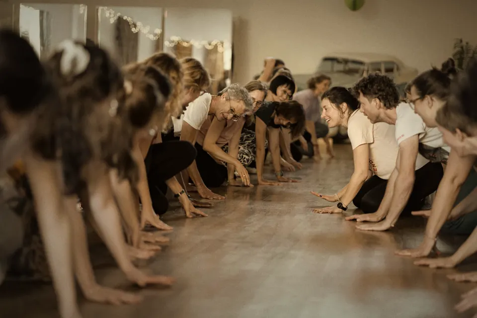Atelier : deux rangées de danseurs penchés, mains au sol, se sourient