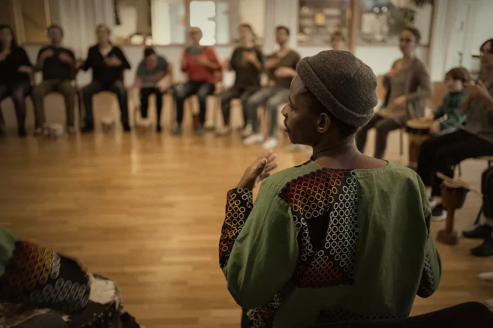 Atelier percussions : une personne en bonnet et tunique verte face à un cercle de chaises